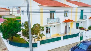 Un edificio de dos pisos con techo de tejas rojas, paredes blancas y contraventanas verdes.