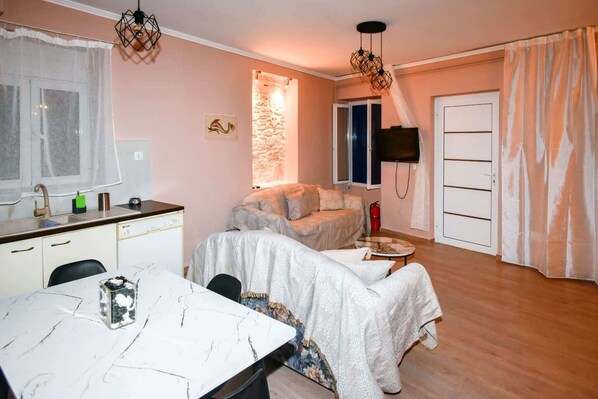 A compact living space with a dining area, a sofa, a TV mounted on the wall, and a stone wall feature.