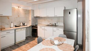 Una cocina compacta con gabinetes blancos, un refrigerador de acero inoxidable, un horno empotrado y una zona de comedor con una mesa y sillas de mármol.