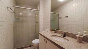 A bathroom with a glass-enclosed shower, a toilet, a sink with a marble countertop, and a mirror. - Nui Supreme Beach Living  (Ipojuca)