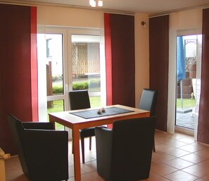 Een eetgedeelte met een tafel en stoelen, een schuifdeur naar een terras en uitzicht op een omheinde tuin.