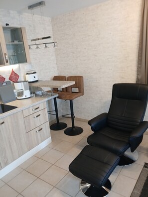 A modern kitchen with a dining area, including a black lounge chair, wooden bar stools, and a small table. - Holiday Apartment '2' with Wi-Fi (Olpe)