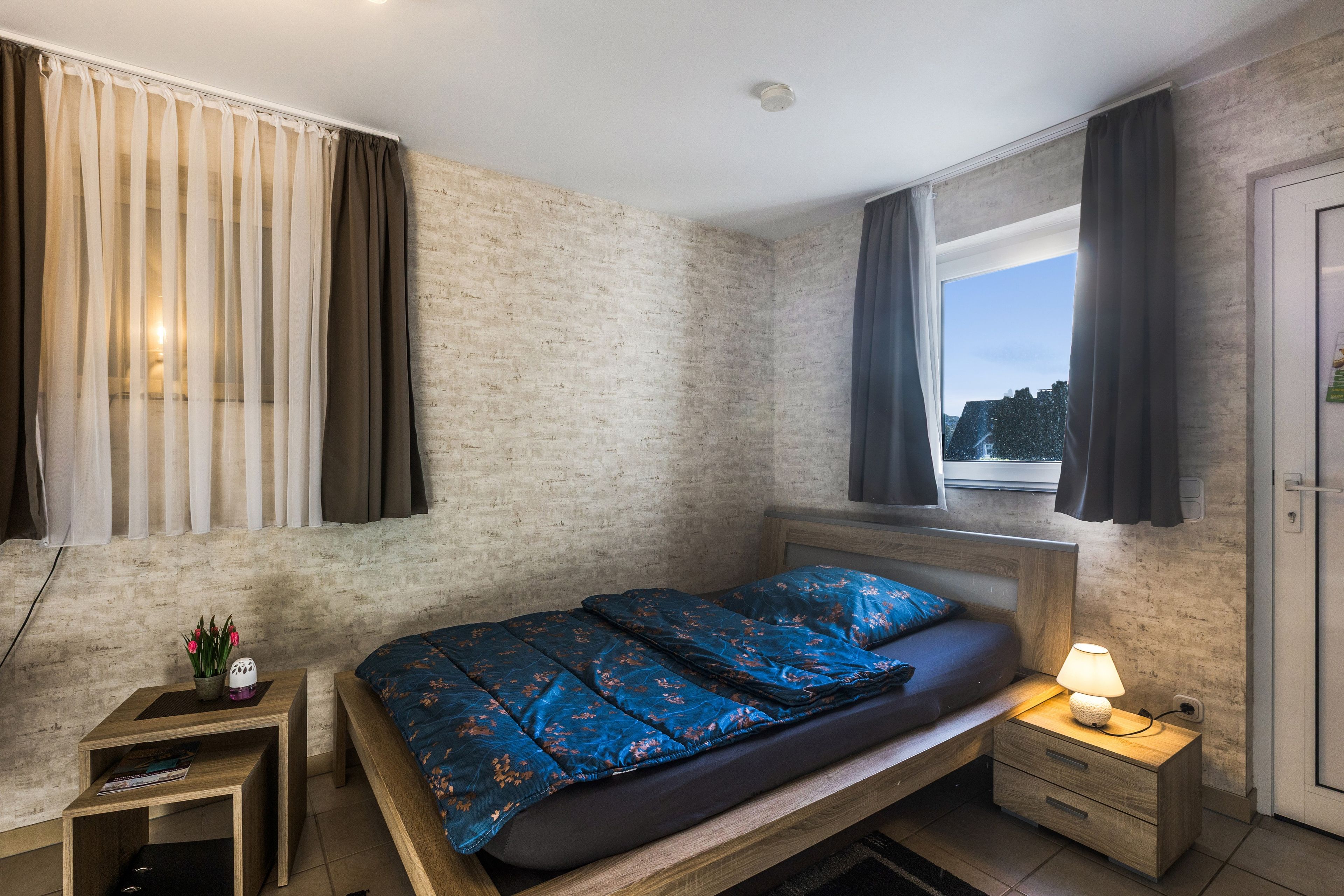 Une chambre à coucher avec un lit, des tables de chevet, une fenêtre avec des rideaux et une vue sur l’extérieur.