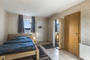 A bedroom with a bed, a window with curtains, a door, and a radiator.