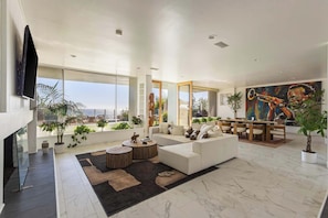 A spacious living room with a large sofa, a dining area, and a view of the city.