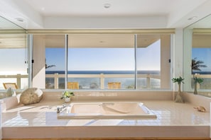 A bathroom with a large bathtub, a window with a view of the ocean, and a potted plant.