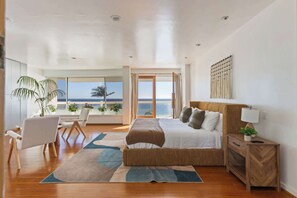 A bedroom with a bed, a desk, a chair, a bedside table, a lamp, and a view of the ocean. - Casa Azul by Oraklus (Malibu)