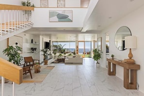 A spacious living area with a staircase, seating, and a view to the outside.