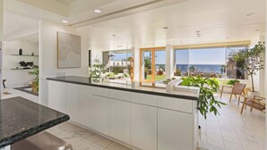 Una cocina moderna con armarios blancos, encimera de granito y vistas a un patio con mobiliario exterior y al mar.