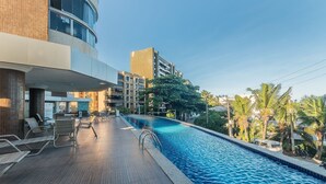 A swimming pool with lounge chairs and a view of surrounding buildings and palm trees. - Live Salvador in Style! (Salvador)