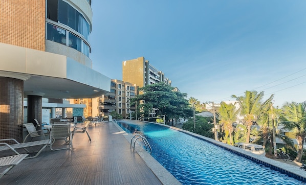 A swimming pool with lounge chairs and a view of surrounding buildings and palm trees.