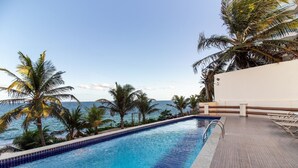 A swimming pool with a view of the ocean, surrounded by palm trees and a white building. - Live Salvador in Style! (Salvador)
