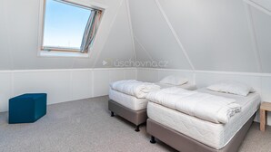 Une chambre avec deux lits, une fenêtre et un pouf bleu.