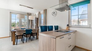 Une cuisine moderne dotée d’un îlot central, d’un coin repas avec des chaises et de grandes fenêtres.