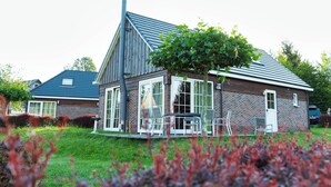 Une maison à deux étages, avec un toit en pente, de grandes fenêtres et une cheminée bien visible.