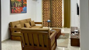 Uma sala de estar com sofá, mesa de centro, televisão e um quadro na parede.