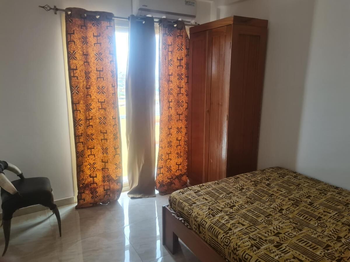 Een slaapkamer met een bed, gordijnen, een stoel en een kledingkast.