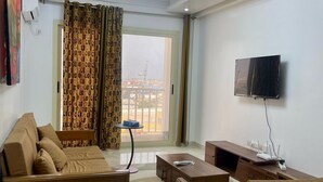Sala de estar moderna com sofá, mesa de centro e televisão. Há uma janela grande com cortinas e vista para o exterior.