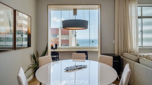 Ein moderner Essbereich mit einem runden Tisch, Stühlen und einer Pendelleuchte. Ein großes Fenster bietet Blick auf das Meer.
