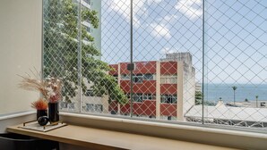 Ein Fenster mit Blick auf ein Gebäude, das rote und beigefarbene Außenwände, einen klaren Himmel und ein Gewässer in der Ferne zeigt.