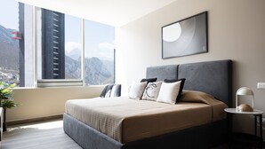 A modern bedroom with a large bed, a bedside table, a nightstand, a window with a mountain view, and a framed artwork on the wall. - 17th-Floor Huasteca Mountain Views, Pool & Gym (21 de Marzo)