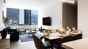 A modern hotel room with a dining area, a flat-screen TV, and a large window offering a mountain view. - 17th-Floor Huasteca Mountain Views, Pool & Gym (21 de Marzo)