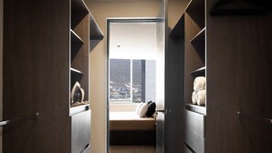 A walk-in closet with open doors, a bed with pillows, and a view of a city through a window. - 17th-Floor Huasteca Mountain Views, Pool & Gym (21 de Marzo)
