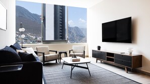 A modern living room with a large window, a flat-screen TV, a sofa, a coffee table, and a minimalist cabinet. - 17th-Floor Huasteca Mountain Views, Pool & Gym (21 de Marzo)