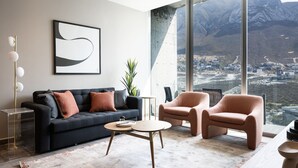 Una sala de estar moderna con un ventanal grande, un sofá negro, una mesa de centro redonda y un sillón rosa.
