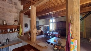 A rustic kitchen with wooden beams, a dining area with a chandelier, and a stone wall. - House, gîte, apartment, private mansion with character historic center Pézenas (Pézenas)