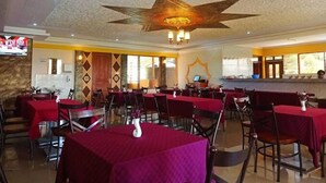 Un restaurant où les tables sont recouvertes de nappes rouges, où le plafond est décoré de motifs en forme d’étoile, et qui dispose d’un bar avec un écran d’ordinateur.