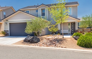 A residential house with a garage, a landscaped front yard with rocks and shrubs, and a small tree.