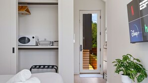 Habitació d'hotel amb llit, microones, taula petita, planta en test i porta corredissa que dona a una zona exterior.