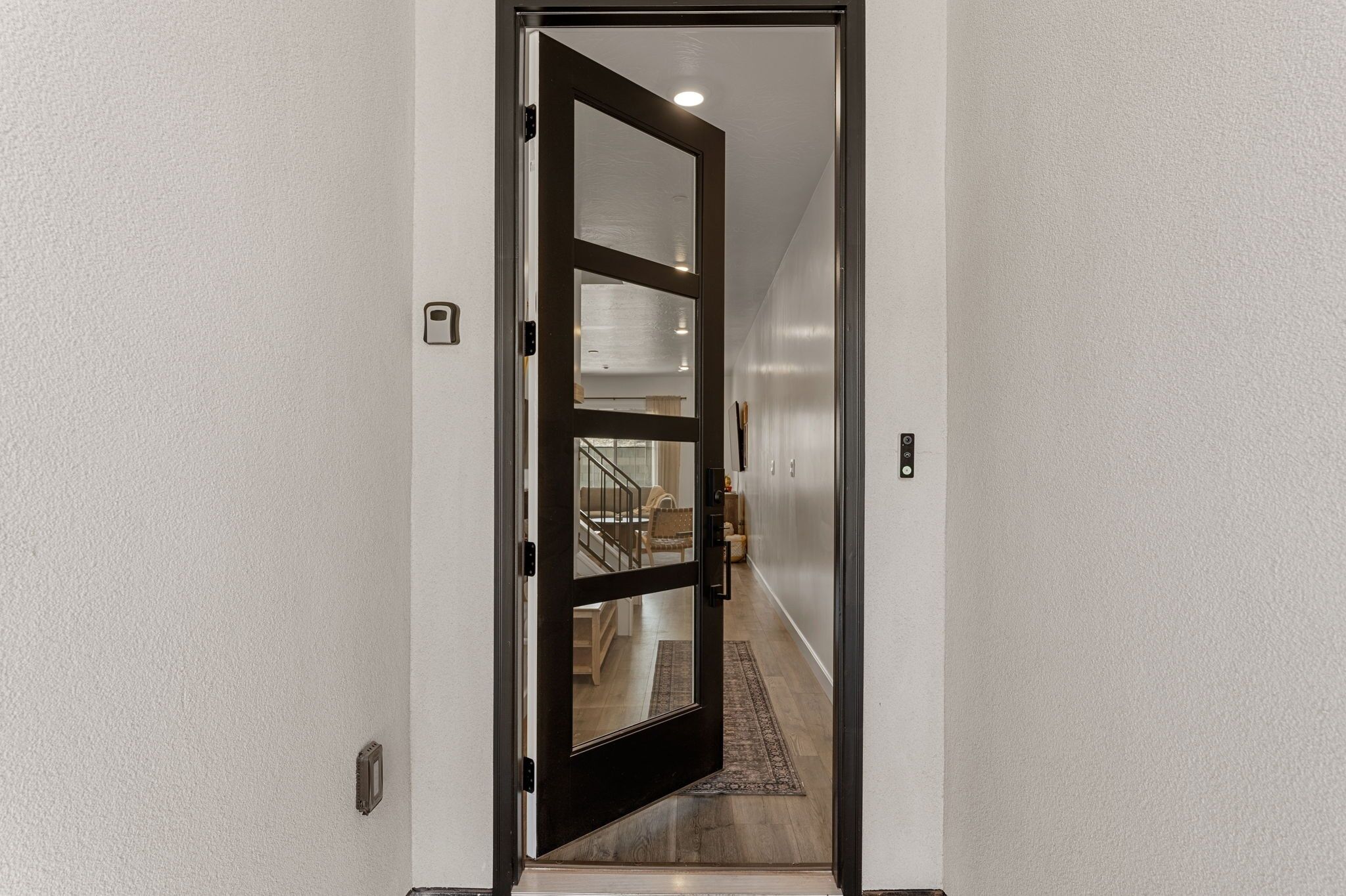Un corridoio con una porta in legno che conduce a una stanza con una scala e vista su un soggiorno.