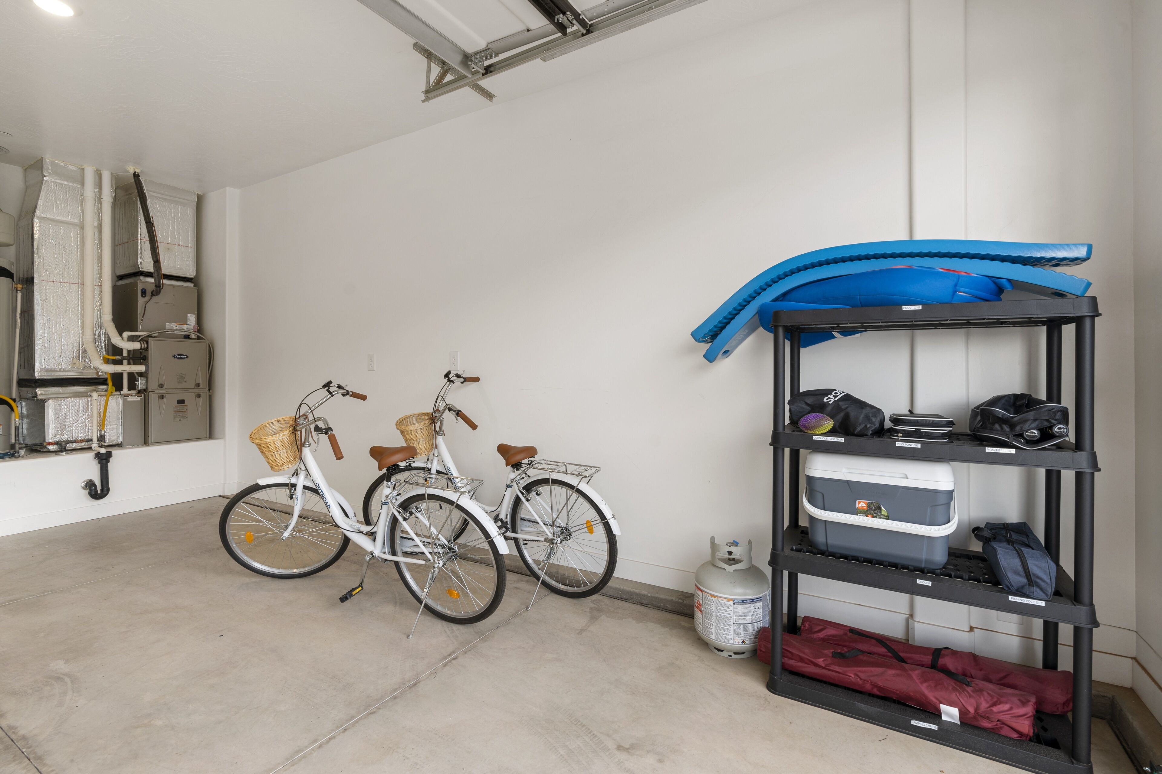 A garage with two bicycles, a gas cylinder, and a storage rack with bags and a cooler.