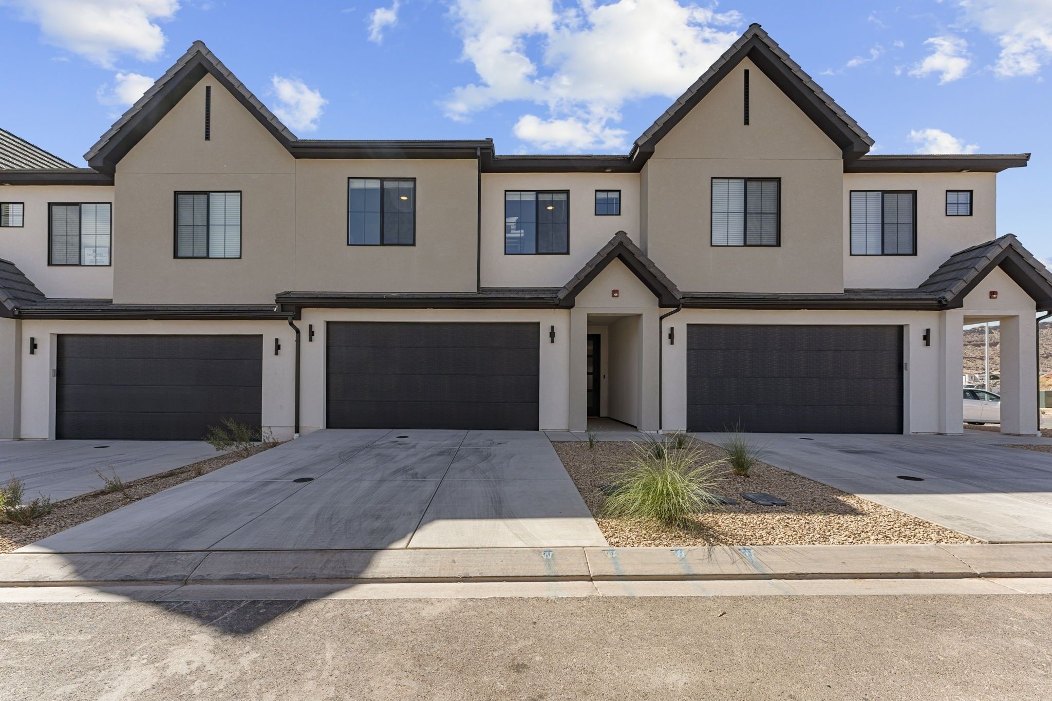 A modern two-story house with a garage, a driveway, and a small landscaped area with plants.