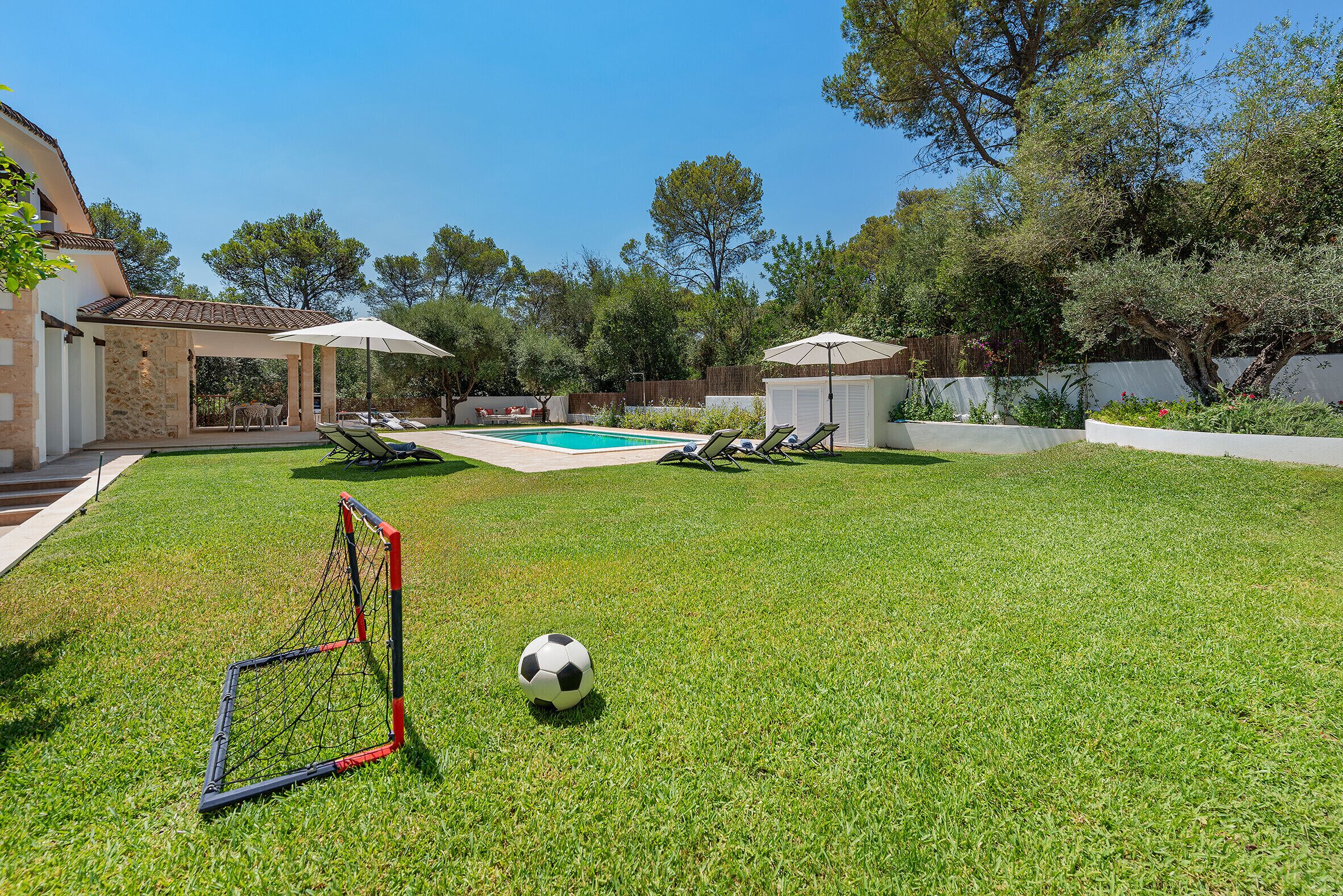 Ein Garten mit Pool, Fußballtor und Liegestühlen.