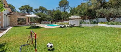 Ein Garten mit Pool, Fußballtor und Liegestühlen.
