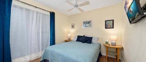 A bedroom with a bed, a ceiling fan, a TV, and a window with curtains.