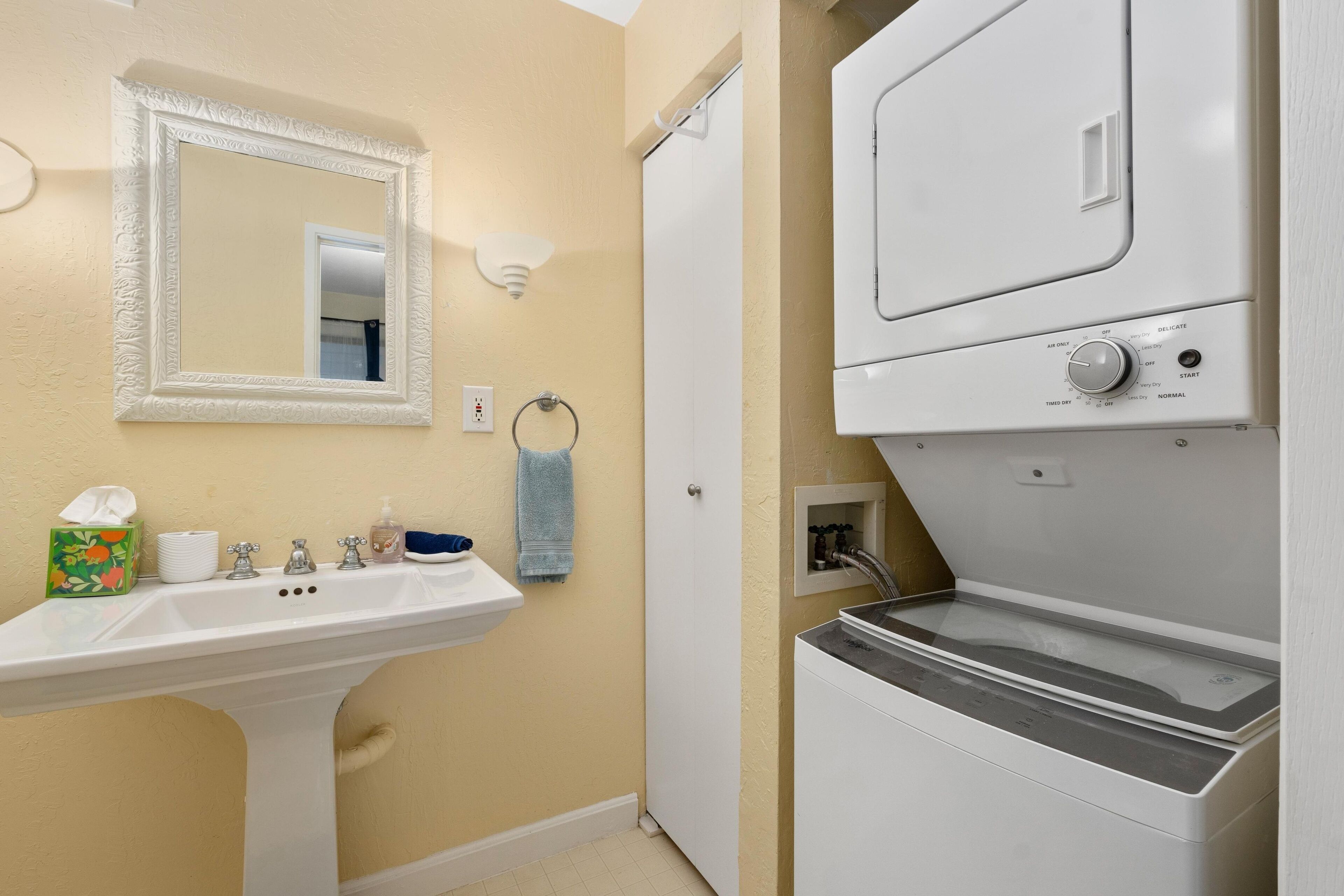 A bathroom with a sink, mirror, towel rack, and a washing machine.