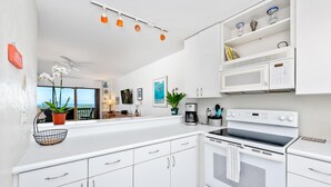 A modern kitchen with white cabinets, a black stove, and a microwave above the counter. - Big Island Kona Westwind 12 2 Bedroom Condo (Kailua-Kona)