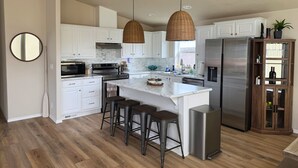 Una cocina moderna con armarios blancos, electrodomésticos de acero inoxidable, una isla grande con taburetes de bar e iluminación colgante.