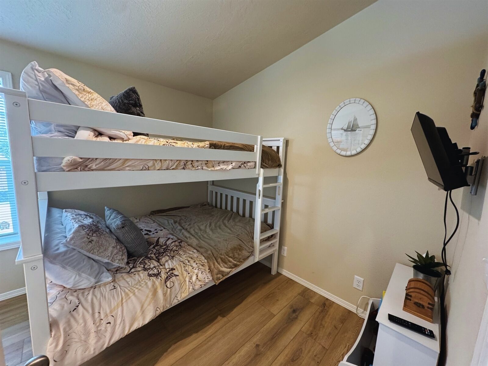 A bunk bed room with a clock on the wall and a TV mounted on the wall.