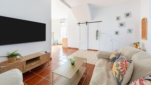 Una sala de estar con una televisión de pantalla plana, un mueble bajo para televisor de madera, un sofá, una mesa de centro y una puerta que da a otra habitación.