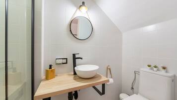 Un baño con tocador de madera, espejo redondo, lavamanos blanco, inodoro y toallero.