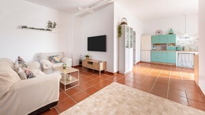 Una sala de estar con sofá, televisor, mesa de centro y una zona de cocina con armarios y mostrador.