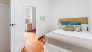 Un dormitorio con una cama, una puerta que da a otra habitación y suelo de baldosas.
