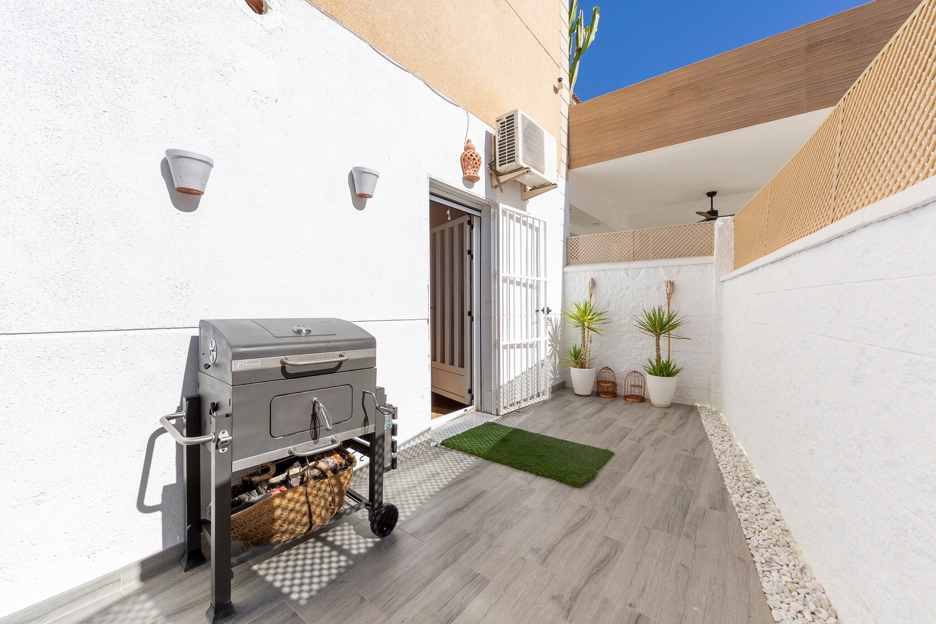 Un patio con una parrilla, plantas en macetas y techo de madera.