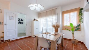 Un comedor con una mesa, sillas, una lámpara colgante, una ventana con cortinas y una planta en maceta.