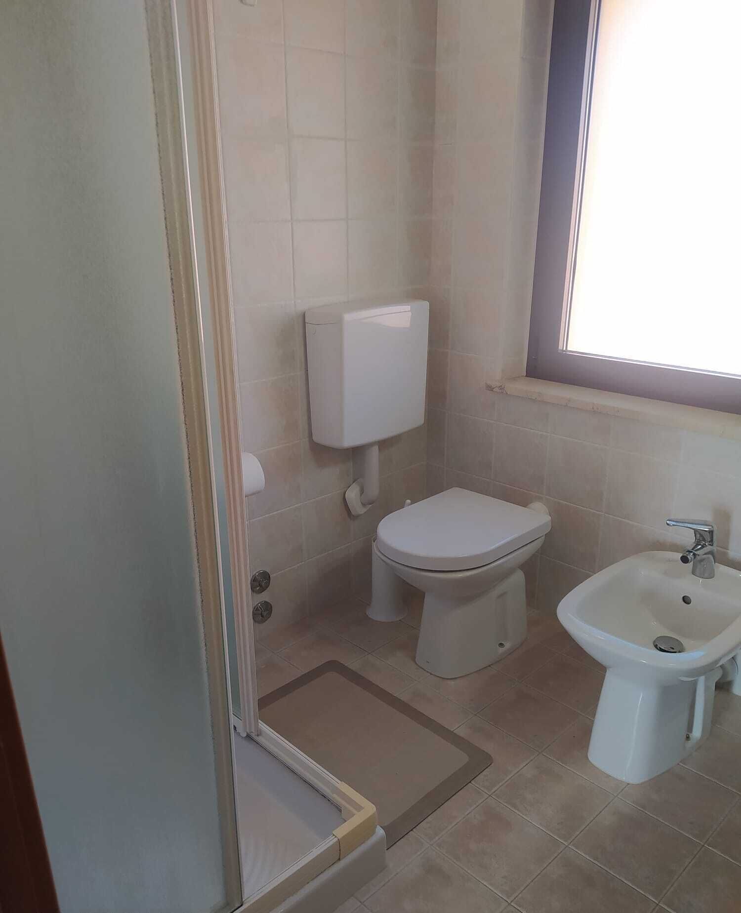 A bathroom with a toilet, bidet, and a window.
